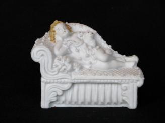 [Reclining child on daybed with cat parian figurine]