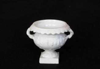 [Vine-handled parian urn on block pedestal base with scalloped leaf lip and low relief grape cluster and leaf patterns]