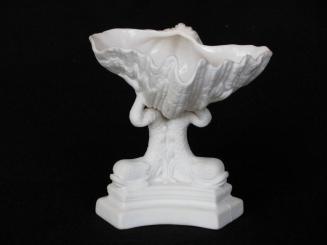 [Clam shell parian vase atop three dolphin ornaments' tails on triangular shaped block pedestal