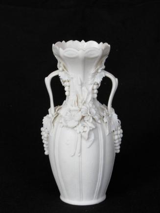 [Amphora-shaped parian vase with two handles, wide mouth with scalloped lip and glazed interior fluting and mottling on neck; applied floral and grape clusters around handles and neck]