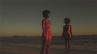 [Two young Black women standing apart on beach at twilight, both are wearing orange/red garments]