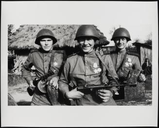 Three proud young soldiers posing in front of thatched hut