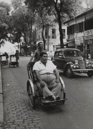 Poverty and wealth in Vietnam: Rickshaw driver with overweight passenger on Catinat Street