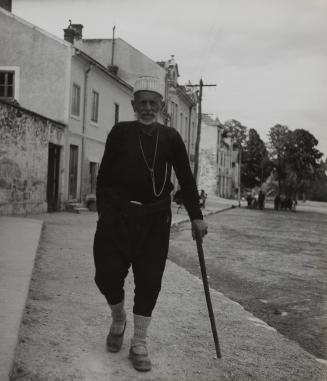 Rich old farmer with a walking stick walking along a street in Tirana, Albania