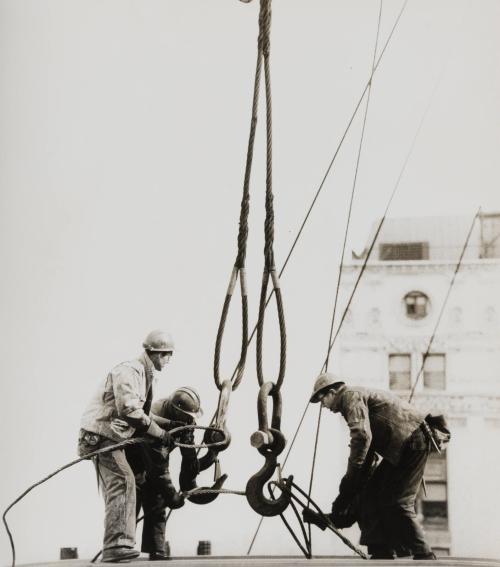 Three construction workers tying ropes on crane hooks