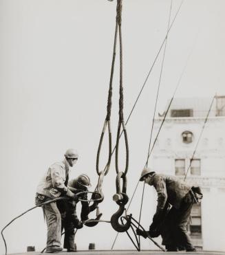 Three construction workers tying ropes on crane hooks