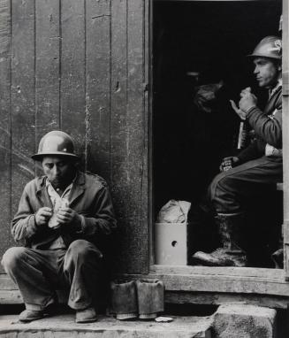 Two construction workers eating lunch by door