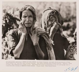 Two women hold scarves over their heads, one crying, one balancing a baby on her torso. 
