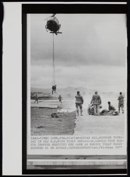 American GIs, wounded in old U.S. minefield explosion, dangle from rescue chopper arriving Khe Sanh as medics treat badly wounded GI on runway, February 1971