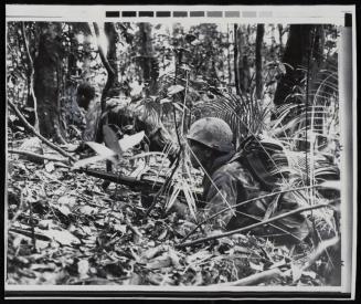A U.S. Marine loses his helmet as he ducks behind a tree as a second marine hugs the ground, his M16 rifle alert, after being fired upon by an undetermined number of North Vietnamese soldiers in the jungle southwest of Da Nang, South Vietnam, the action took place near an enemy regimental base camp on April 22, 1969