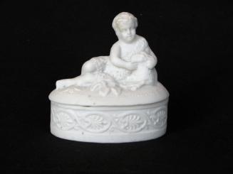 [Lidded oval-shaped parian box with shepherd and lamb figurine on lid and low relief floral and vine design with mottled background on box]