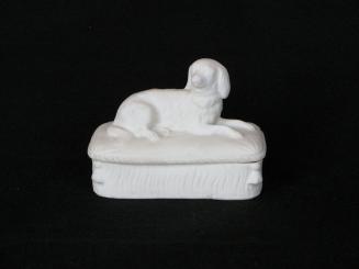 [Lidded parian box with reclining dog on cushion-motif lid and high relief tassels on box]