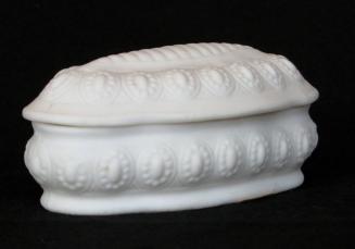[Oval-shaped lidded parian trinket box with low relief segmented design on lid and high relief bead-and-oval repeating pattern on lid and box]