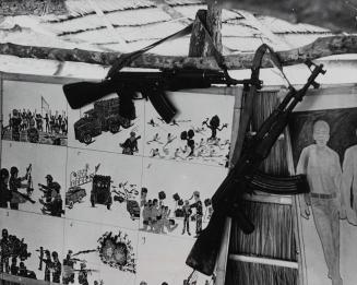 Guns hang in front of drawings of war scenes, Cambodia, c. 1980