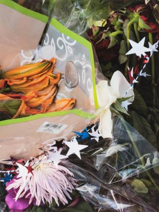 [Flowers wrapped in plastic and string of patriotic stars]