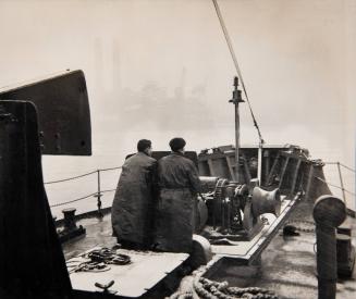 [Sailors on boat with factory in the background]