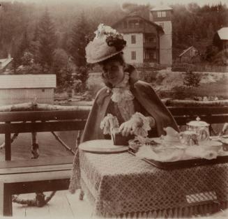 [Woman with floral hat sits at table]